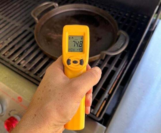 Людина, яка використовує жовто-чорний ІЧ-пістолет ThermoWorks для вимірювання температури сковороди на грилі