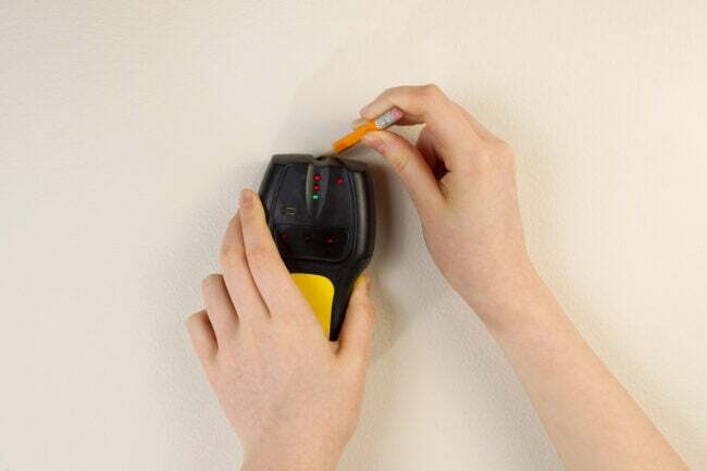 Cum să ancorați mobila pe perete femeie folosind instrumentul de căutare pentru a localiza și a marca știftul pe perete