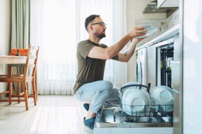 Одрасли мушкарац истоварује машину за прање судова