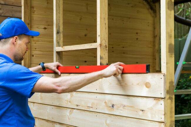 يستخدم الإنسان مستوى لبناء سقيفة خشبية