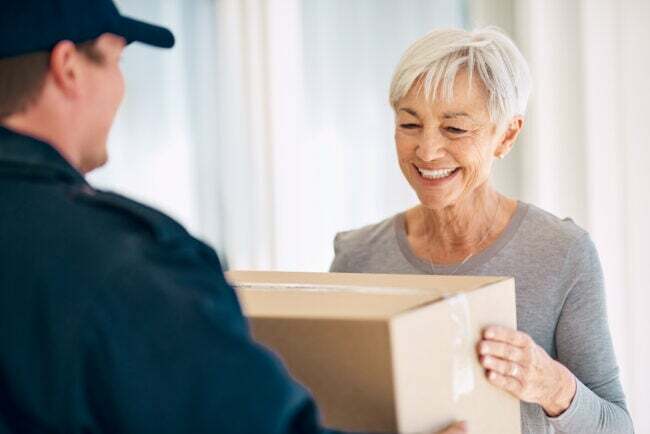 Uma mulher idosa aceitando entrega de um mensageiro em sua casa.