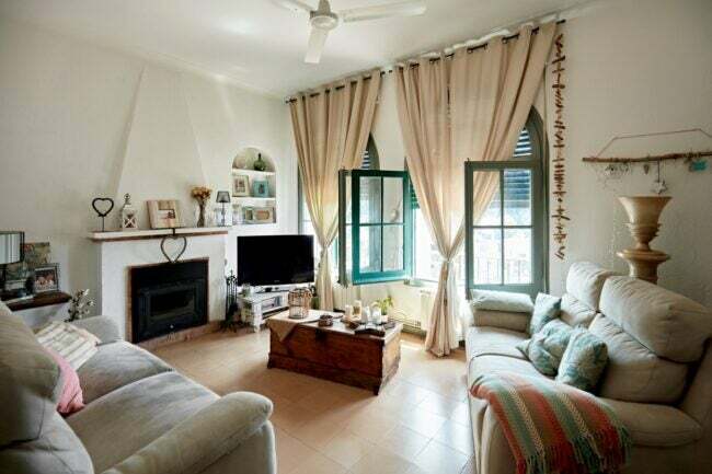 Ruang tamu yang nyaman dengan sofa, perapian, dan tirai setinggi langit-langit