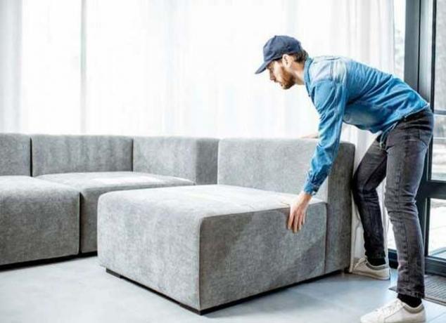 Hombre moviendo parte de un sofá seccional gris
