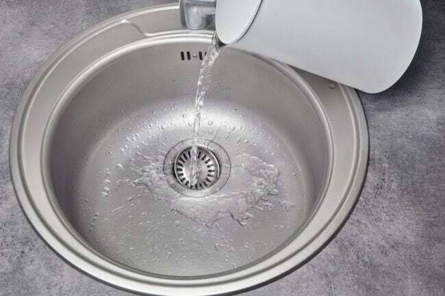 Vruća voda teče iz bijelog električnog kuhala za vodu u metalni sudoper
