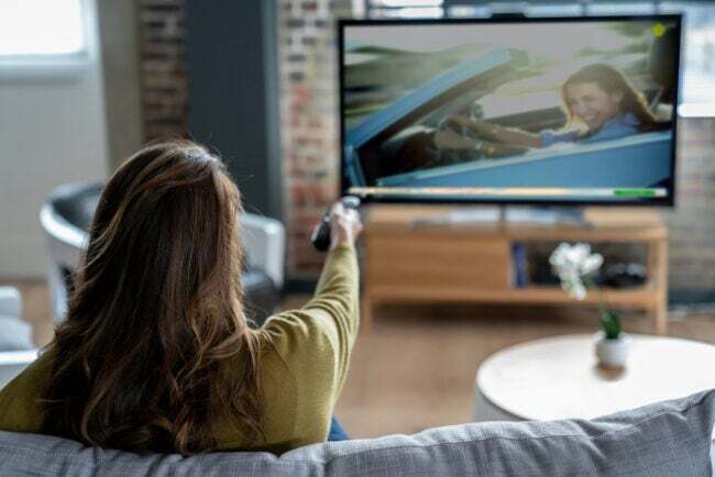 Kvinna som pekar fjärrkontrollen mot vardagsrummet stor TV