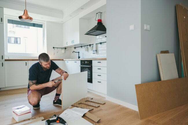 Чоловік на корточках працює над ремонтом кухні.