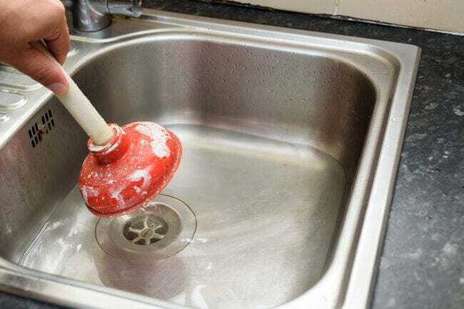 Bărbat folosind un piston cu o mână și apă în chiuveta de bucătărie.