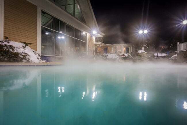يتصاعد البخار من أعلى حوض السباحة ليلاً في الفناء الخلفي الثلجي.