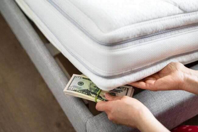 Person legt einen Stapel Geld unter die Ecke einer Matratze