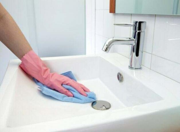 Fürdőszoba mosdót takarító személy rózsaszín gumikesztyűt visel