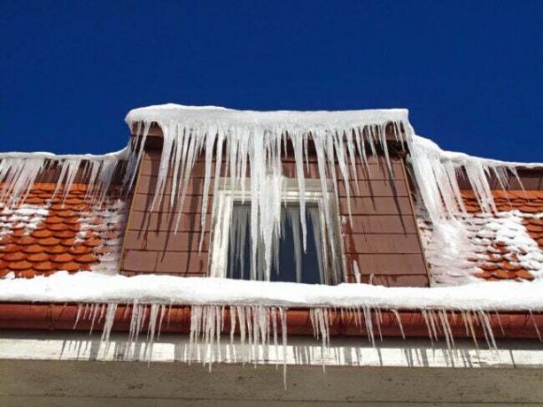 I ghiaccioli pendono da un tetto di tegole rosse.