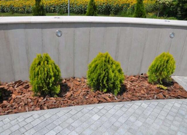 Planteseng af murstensspåner med grønne buske plantet i, omgivet af grå murstenssti. 