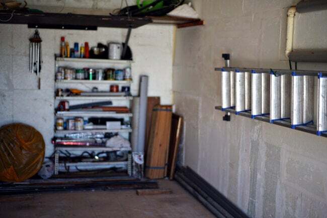 garagem interna com paredes de tijolos brancos com escada montada na parede e uma prateleira na parte de trás com latas de tinta armazenadas