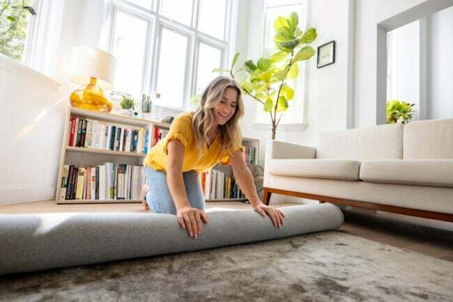 Vrouw die dik tapijt in de woonkamer uitrolt.