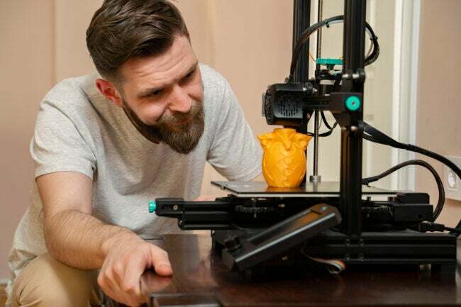 iStock-1316154786 zarábajte peniaze s 3D tlačiarňou Muž sleduje, ako 3D tlačiareň vytvára sovu.jpg