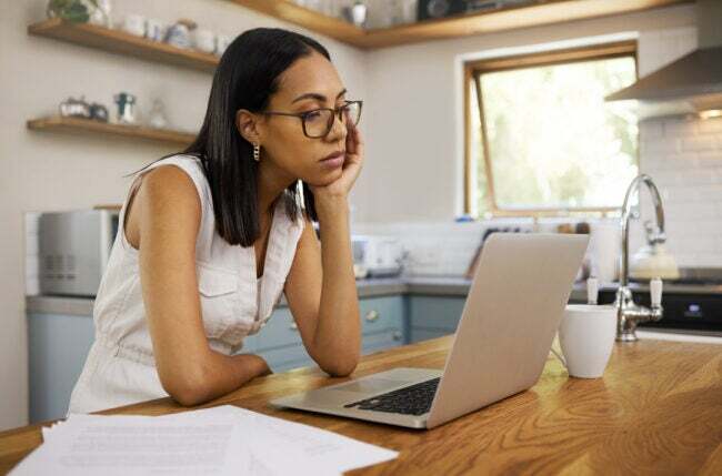 жінка, розчарована через погане підключення до Інтернету, дивлячись на ноутбук, що працює на кухні