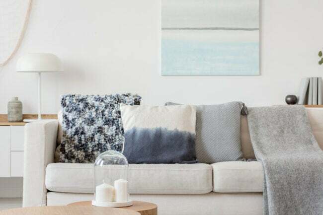 明るい色のリビング ルームに白いソファ、青い枕と毛布