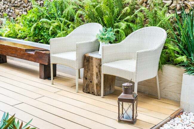 dwa białe krzesła patio na pokładzie obok drewnianej ławki z paprociami w kształtowaniu krajobrazu za nimi obok ścieżki skalnej