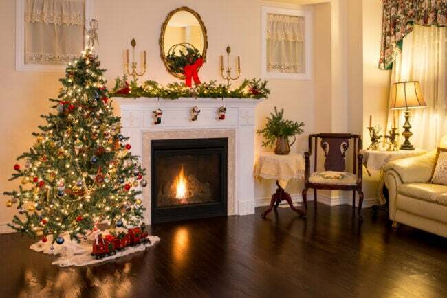 Antiikkihuonekalut, joulukuusi ja kupariset kynttilänjalat perinteisessä jouluksi sisustetussa huoneessa.
