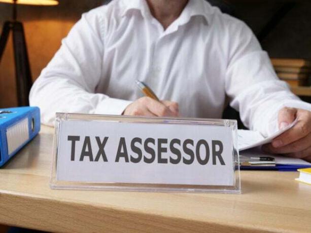 Mężczyzna w białej koszuli przy biurku z napisem „administrator podatkowy” na biurku.