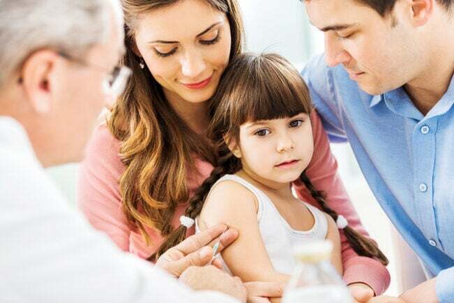 jauna meitene ar saviem vecākiem vakcinējas pie ārsta, kurš vērš adatu pret viņas roku