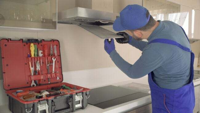 Servicemann in blauer Uniform öffnet Dunstabzugshaube in der Küche, um den Ventilator zu überprüfen