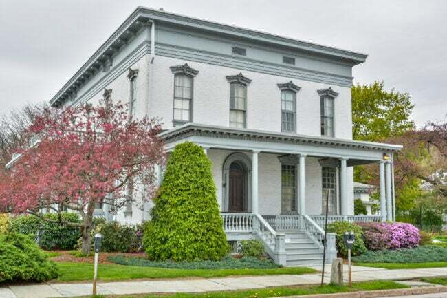 Una-casa-histórica-gris-pálido-está-rodeada-de-un-diseño-de-paisaje-verde-y-rosa.