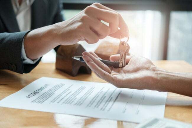 Agent nieruchomości daje człowiekowi klucze do domu i podpisuje umowę w biurze