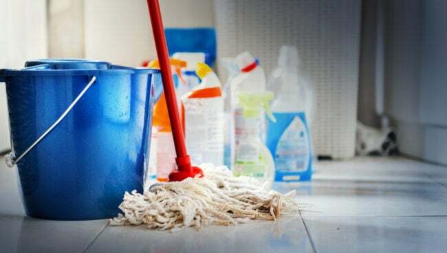 En blå spand, rengøringsmidler og en moppe ses på et flisegulv.