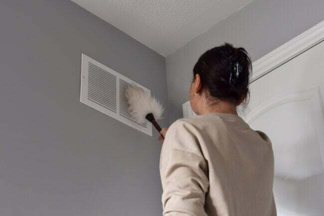 Жена почиства вентилационния отвор за обратен въздух с кърпа за прах