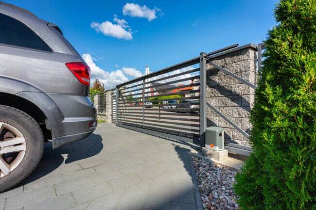 Сріблястий автомобіль припаркований на під’їзді із закритими воротами.