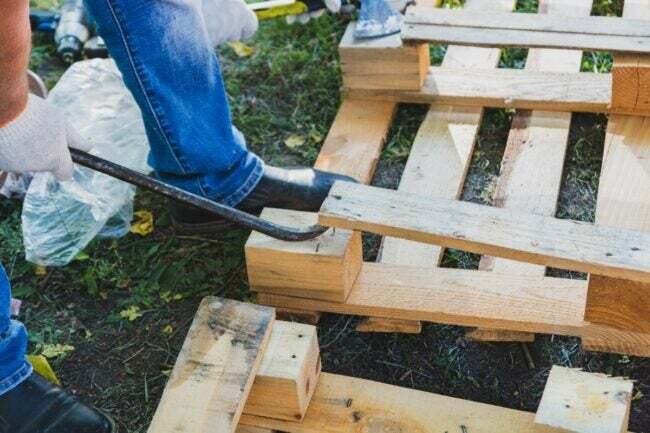 Mann benutzt Brecheisen, um eine Holzpalette auseinanderzubrechen