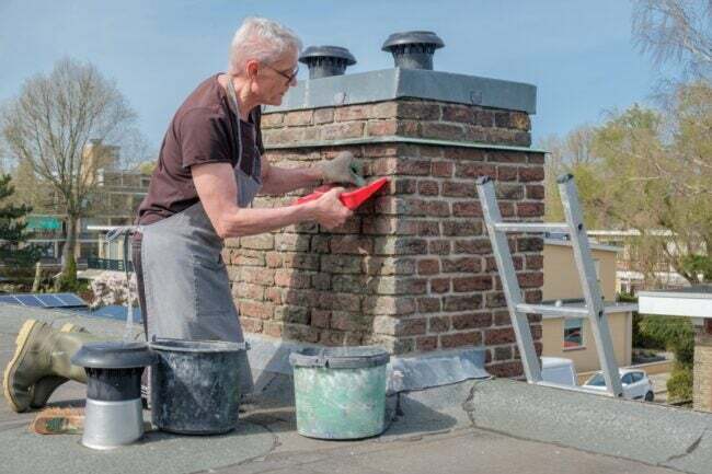 Homem consertando chaminé externa de tijolos