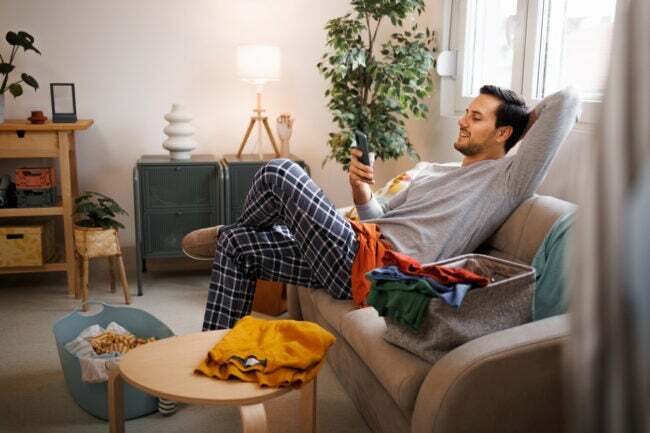 iStock-1435987105 hacks de procrastinação homem relaxando em vez de fazer tarefas domésticas