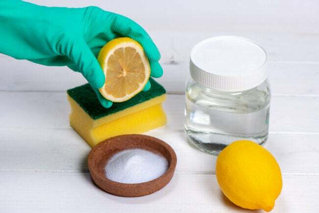 Persona che indossa guanti che tengono il limone tagliato, con spugna, limone, sale e un barattolo di liquido.