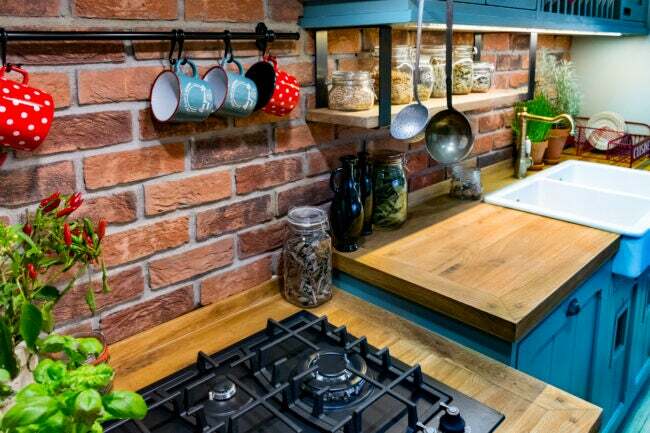Стільниця з м’ясного блоку з відкритою цегляною стінкою, свіжою зеленню та підвішеними кухлями та посудом