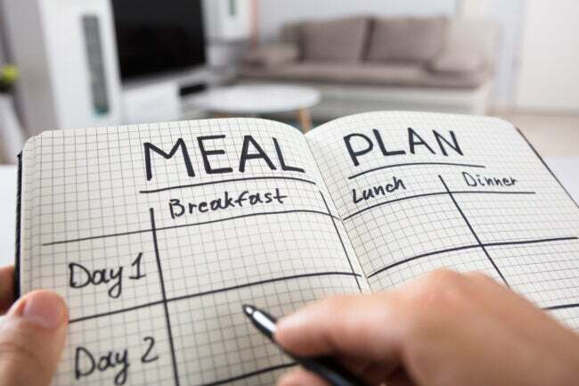 Близък план на план за хранене с пълнене на човешка ръка в кариран бележник