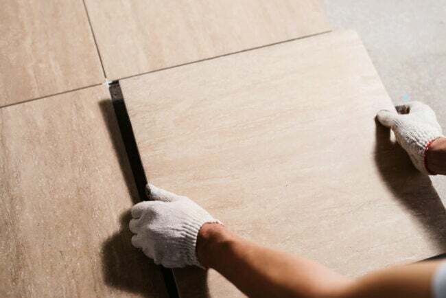 Mãos enluvadas instalando piso de cerâmica