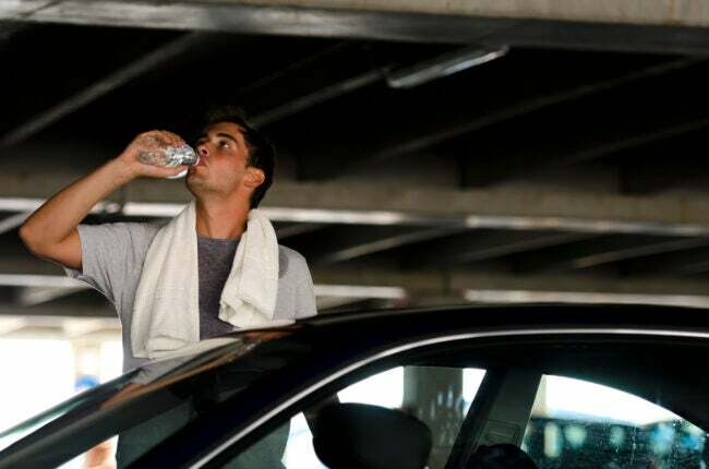 moški, ki stoji zunaj svojega avtomobila in se hladi z brisačo in steklenico vode