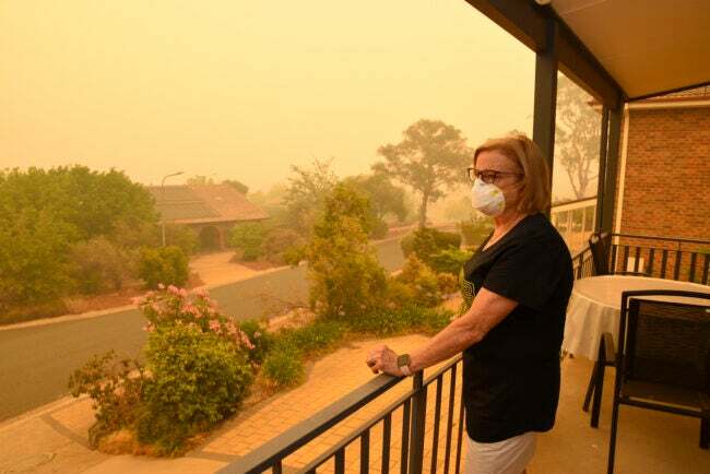 Eine Frau, die eine Gesichtsmaske trägt, blickt auf die Nachbarschaft, in deren Luft Rauch von Waldbränden liegt