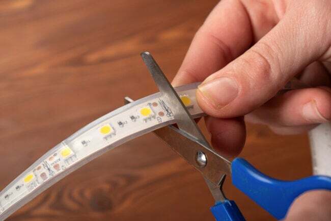 Close de uma demonstração de como cortar uma faixa de luz LED com uma tesoura de segurança
