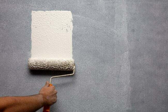 Person, der bruger malerrulle til at male primer på en mørk væg