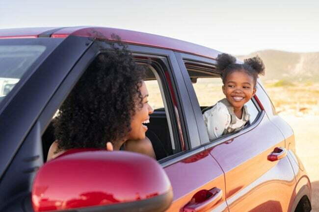 moeder leunt uit de bestuurderskant van het raam van een rode SUV en kijkt naar dochter in het raam op de achterbank in woestijnlandschap