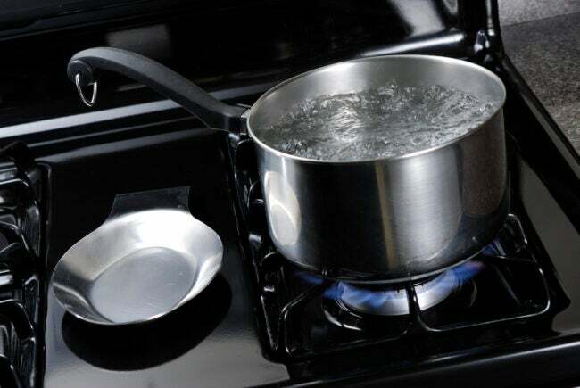 Vatten som kokar i en rostfri kastrull på en svart spis.