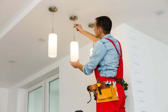 iStock-1263134450 vergi iadesi ev iyileştirmeleri Elektrikçi adam işçi tavan lambası takıyor