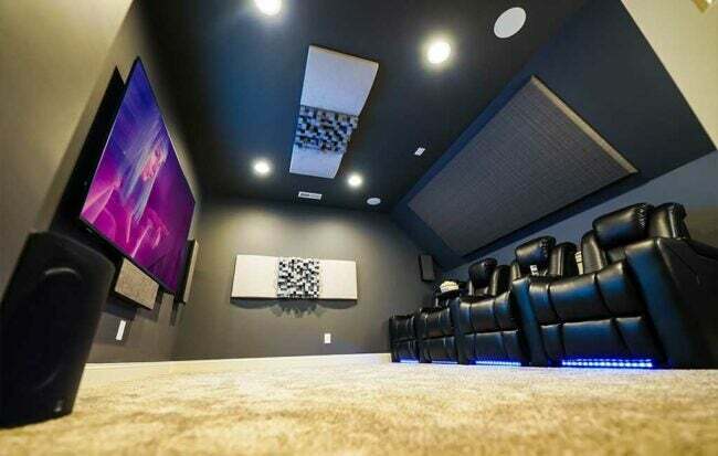 Dört siyah deri koltuklu küçük ev sineması, akustik panel, büyük TV