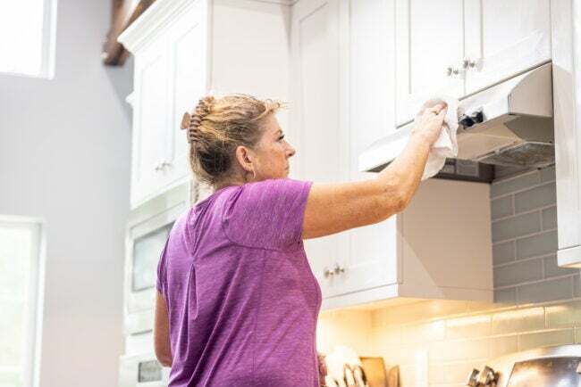 ženska v vijolični majici s krpo čisti belo kuhinjsko napo