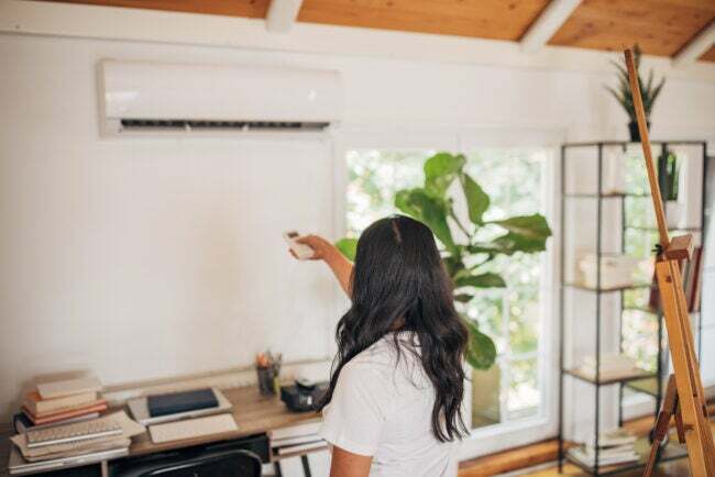 kvinne på hjemmekontoret bruker fjernkontrollen for å slå på klimaanlegget montert på veggen