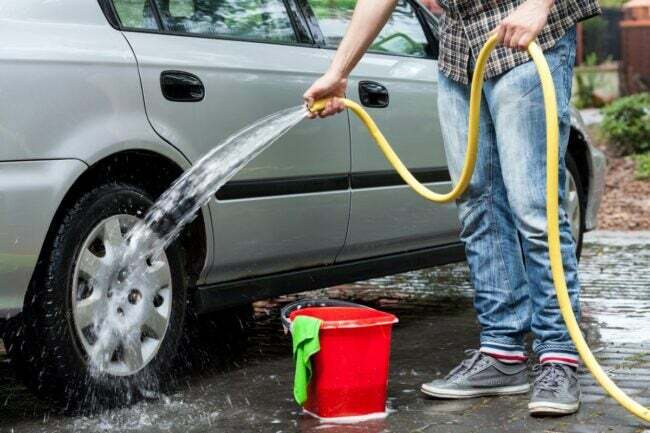 autókarbantartási feladatok - személy, aki tömlőt használ az autó tisztításához