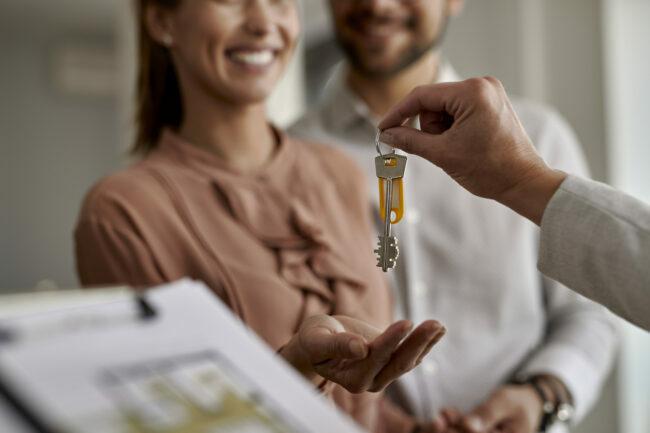 Iš arti matomas nekilnojamojo turto agentas, kuris porai dovanoja naujus namų raktus.